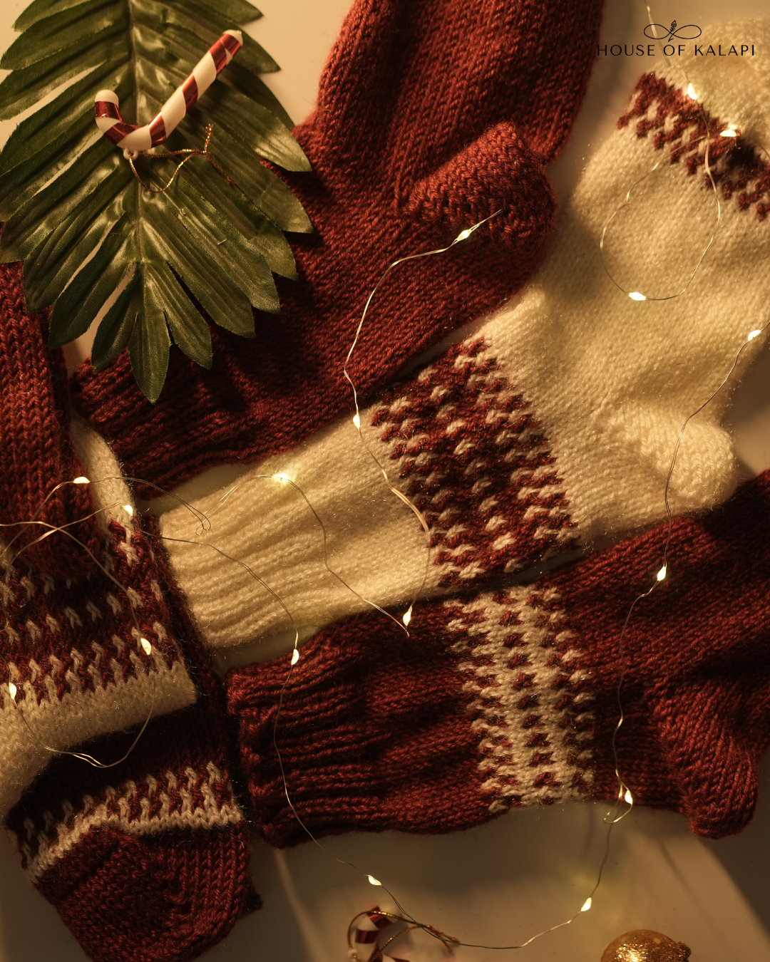 Three hand-knit wool socks in cream and maroon with festive lights and décor — artisan-made Christmas gift set.